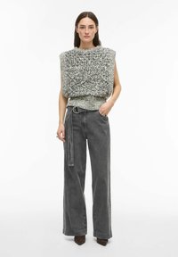 Tjockstickad grå och svart ärmlös topp med rund halsringning, kombinerad med högmidjade, vida mörkgrå jeans med bältesdetalj.