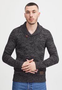 Gestrickter schwarzer und grauer Pullover mit Schalkragen, Holzknopf-Detail, strukturiertem Stoff und gerippten Bündchen, kombiniert mit Jeans.