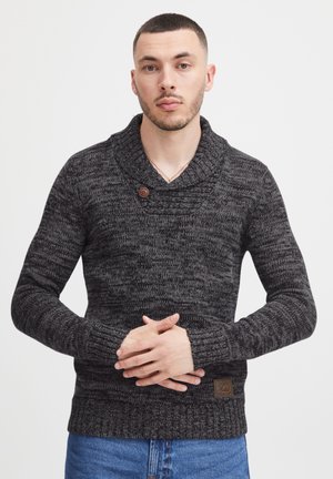 Knitted black and gray sweater with a shawl collar, wooden button detail, textured fabric, and ribbed cuffs, paired with denim jeans.