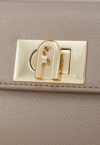 Light beige leather handbag featuring a textured finish, gold-tone hardware clasp with an intricate logo design, and stitched detailing.