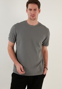 Tricou scurt gri cu mâneci scurte, cu un guler rotund, având o suprafață texturată și o croială lejeră, combinat cu pantaloni negri.