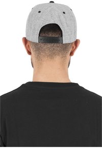 Berretto da baseball grigio con tessuto testurizzato, dettagli neri e chiusura snapback regolabile. Indossato con un leggero angolo.