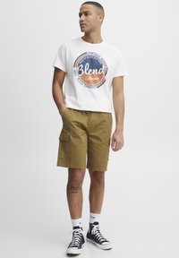 White cotton t-shirt with "Blend California" graphic, paired with khaki cargo shorts featuring side pockets. Black high-top sneakers.