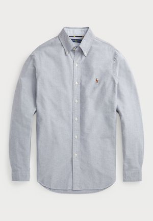 Cămașă lungă, cu mâneci lungi, de culoare bleu deschis, realizată dintr-un material țesut. Are un guler ascuțit, un logo pe piept și nasturi albi.
