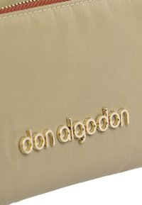 Bolsita de tela beige con una textura suave, que presenta un logo en tono dorado "don algodon". La parte superior tiene un cierre rojo de contraste.