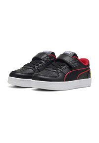 Zapatillas de cuero negro con una línea de acento roja, suela de goma blanca y correa de velcro con detalles perforados en la puntera.
