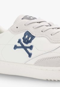 Witte sneaker met grijze suede accenten, voorzien van een blauw geborduurd doodskop en gekruiste botten ontwerp, een getextureerde rubberen zool en lichtgrijze veters.