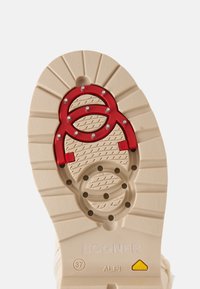 Semelle de chaussure avec un revêtement beige, pointes métalliques rouges pour la traction, taille 37, marque Bogner, et étiquette "Alpi" avec logo jaune.