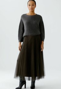 Gray, soft, wool sweater with a wide neckline paired with a black pleated, sheer mesh maxi skirt and black high-heeled boots.
