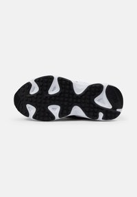 Semelle de sneaker blanche et noire avec un motif de texture antidérapante ; présente des studs circulaires surélevés et un logo près du talon.