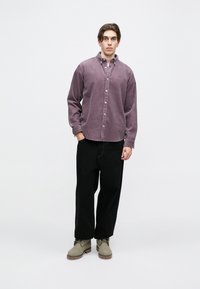 Dlhé rukávy, košeľa s gombíkmi, fialová zamatová košeľa s golierom, v kombinácii s voľnými čiernymi nohavicami a šedými semišovými topánkami.