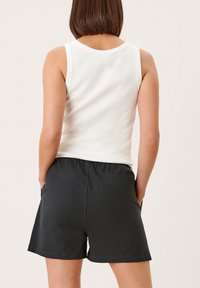 Valkoinen ribattu tanktoppi yhdistetty tummanharmaisiin elastisellä vyötäröllä varustettuihin shortseihin. Shortsien sivuilla on taskut ja ne ovat rentoa muotoilua.