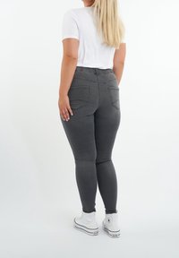 Jeans en denim gris avec une coupe slim, une taille élastique et deux poches arrière. Porté avec un t-shirt blanc et des baskets montantes blanches.