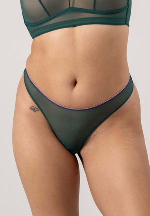 Groene netstring met een laag uitgesneden ontwerp en contrasterende roze details langs de tailleband en een gladde textuur. Subtiel tatoeage-detail zichtbaar.