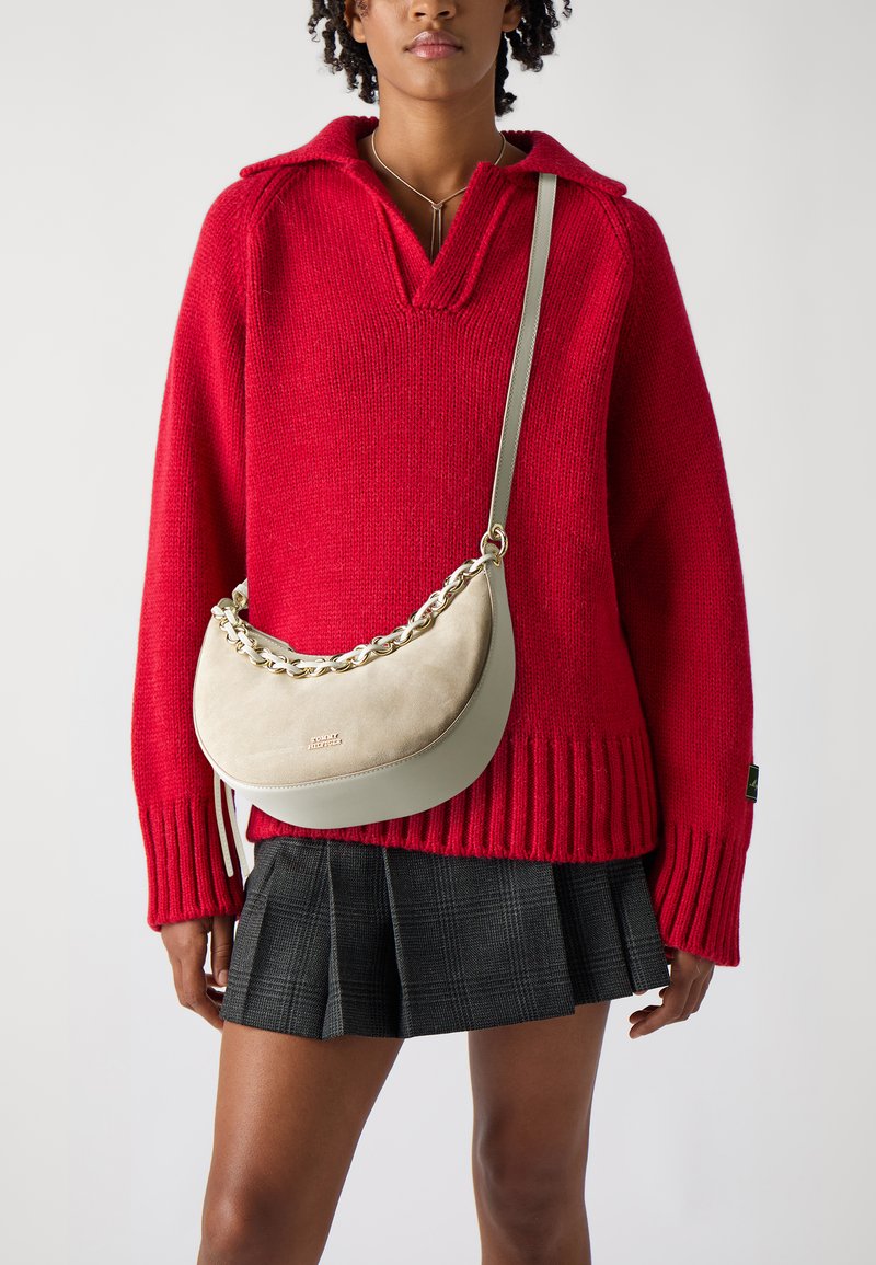 Rød strikket sweater med krave, parret med en plisseret sort ternet nederdel. Lys grå skuldertaske med en tekstureret overflade og kædedetalje.