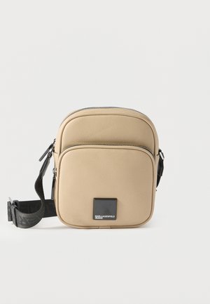 Sac bandoulière compact beige avec poche avant zippée, sangle réglable noire et patch logo carré noir portant l'inscription "Karl Lagerfeld Jeans".