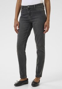 Jeans en denim gris avec une coupe ajustée, poches standard, fermeture éclair, et des détails de couture élaborés le long des coutures.