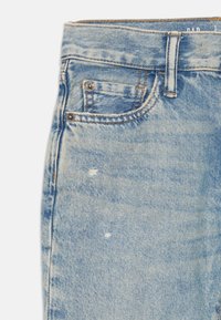 Jeans en denim bleu clair avec une finition décolorée, présentant une poche avant, de petits détails d'usure et des coutures contrastantes.