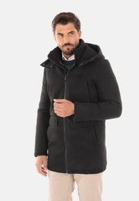 Cappotto nero con colletto alto, chiusura con zip e tasche laterali. Realizzato in tessuto testurizzato, con cappuccio e vestibilità su misura.