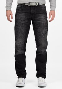 Jeans in denim nero con una finitura sbiadita, caratterizzati da dettagli invecchiati e un design a gamba dritta. Indossati con sneakers bianche e una felpa grigia.