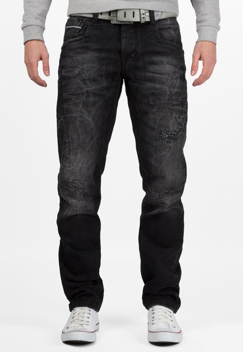 Jeans in denim nero con una finitura sbiadita, caratterizzati da dettagli invecchiati e un design a gamba dritta. Indossati con sneakers bianche e una felpa grigia.