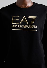 Zwarte sweatshirt met een prominent goudkleurig logo en de tekst "EAZ EMPORIO ARMANI". Gladde stofstructuur met geribbelde kraag.