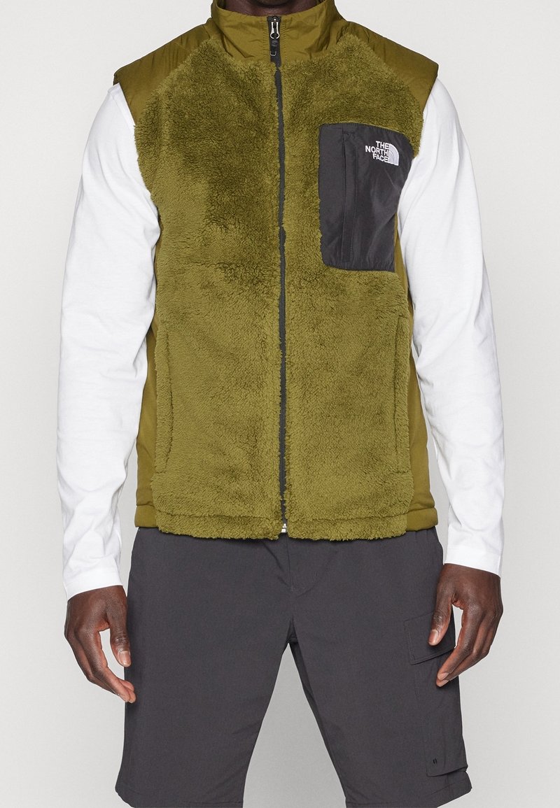 Grön fleeceväst med ett quiltat tyg på toppen och en svart bröstficka. Dragkedjestängning, ställbar krage och detaljer med texturerad yta.