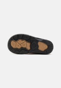 Semelle de chaussure en caoutchouc noir avec un motif texturé, présentant une accentuation marron et divers designs de grip pour la traction et la durabilité.