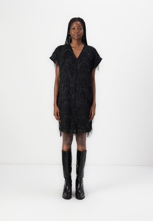 Vestito nero con dettagli frangiati, scollatura a V, maniche corte e forma ad A. Indossato con stivali neri di pelle al ginocchio.