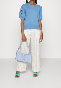 Maglione azzurro chiaro con maniche a sbuffo e dettaglio a taglio, pantaloni a righe bianchi a gamba larga, sandali turchesi con nodi e borsa azzurro chiaro.