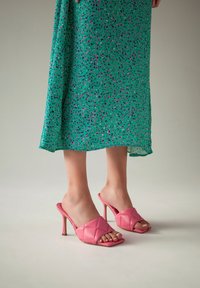 Sandale cu toc roz, cu design matlasat si varf descoperit. Toc stilettos si material din piele neteda. Poarta o rochie cu model verde.