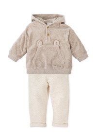 Sudadera con capucha beige con orejas de oso y un bolsillo frontal, combinada con pantalones crema acolchados con manguitos doblados. Textura suave en toda la prenda.