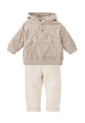 Sudadera con capucha beige con orejas de oso y un bolsillo frontal, combinada con pantalones crema acolchados con manguitos doblados. Textura suave en toda la prenda.