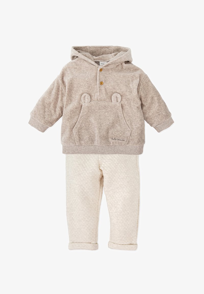 Sudadera con capucha beige con orejas de oso y un bolsillo frontal, combinada con pantalones crema acolchados con manguitos doblados. Textura suave en toda la prenda.