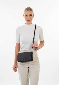 Zwarte faux leren crossbody tas met een gestructureerd oppervlak en gouden metalen accenten. Voorzien van een afneembare, verstelbare schouderriem en een slank rechthoekig ontwerp.
