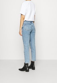 Jean en denim bleu clair de coupe ajustée avec un style cinq poches, assorti à des bottines noires et un t-shirt blanc.