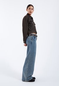 Black cropped denim jacket with buttons, paired with light blue wide-leg jeans and a studded black belt. Smooth texture, casual design.