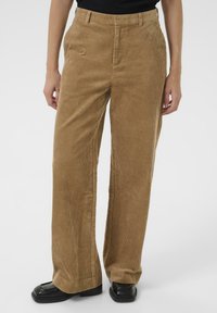 Bruine corduroy broek met een rechte pijp, voorzien van opvallende verticale ribbels en zijzakken, gecombineerd met zwarte platte schoenen.