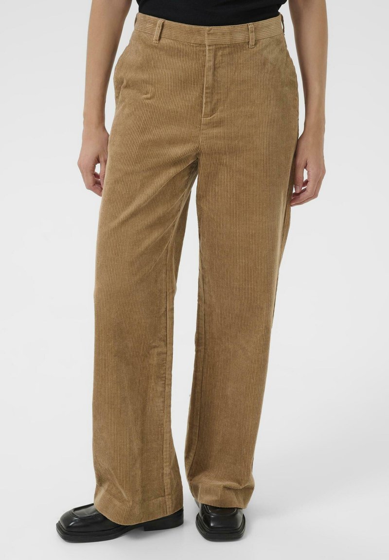 Bruine corduroy broek met een rechte pijp, voorzien van opvallende verticale ribbels en zijzakken, gecombineerd met zwarte platte schoenen.