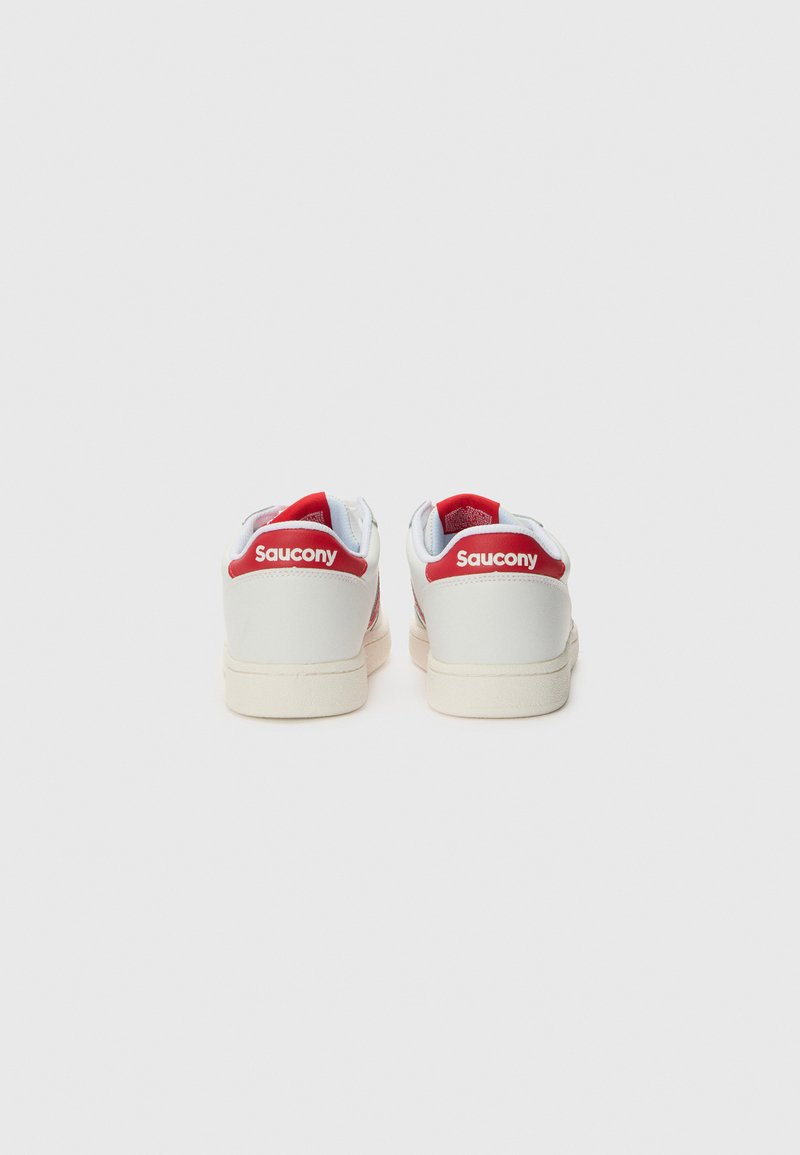 Sneakers in pelle bianca con accenti rossi sul tallone e sul logo. Presentano un design a bassa altezza e suole in gomma testurizzata. Estremità dei lacci visibile.