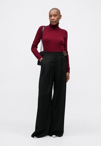 Bordowy sweter z golfem połączony z czarnymi spodniami z wysokim stanem i szerokimi nogawkami z detalem paska. Gładkie tekstury, swobodny styl.