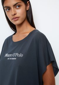 Czarna szara koszulka z luźnym krojem, krótkimi rękawami i białym napisem "Marc O'Polo EST. W STOCKHOLM." Miękka faktura materiału.