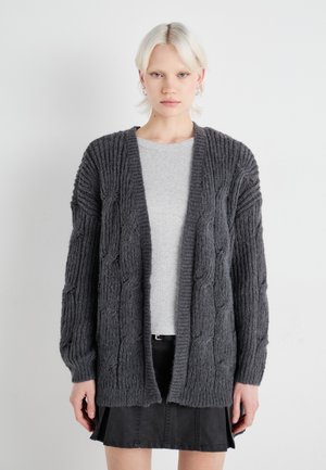 Cardigan oversized grigio scuro con motivo a trecce, maniche lunghe, apertura frontale e tessuto strutturato, indossato sopra un top grigio chiaro.