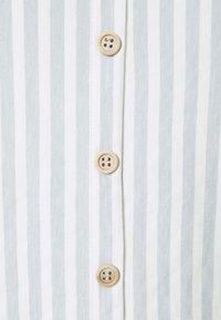 Chemise rayée avec des rayures verticales bleu clair et blanches, dotée de quatre boutons marron sur le devant. Texture en coton ou mélange de coton.