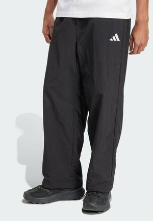 Mustad nailonist püksid lohaka lõikega, mille vasakul jalal on valge Adidas'i logo. Sile tekstuur ja kitsenevad pahkluud.