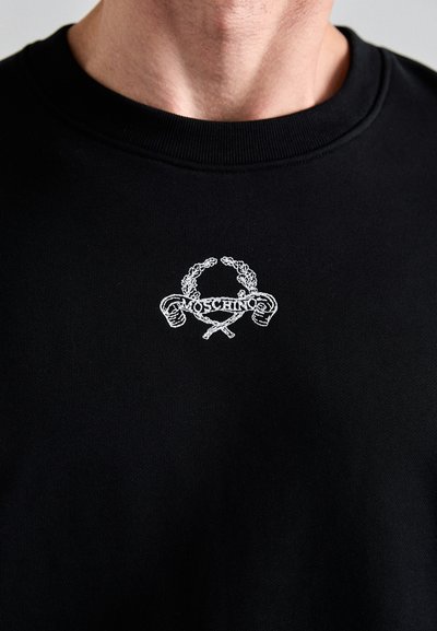 Svart sweatshirt med en vit broderad logotyp med en lagerkransdesign och text, som visar en ribbad krage och textur.