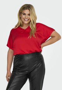 Röd satinblus med V-ringning, korta ärmar och avslappnad passform; kombinerad med högmidjade svarta lädernäbyxor med texturerade detaljer.