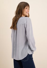 Blusa a maniche lunghe a righe blu e bianche, vestibilità morbida, orlo arrotondante e dettaglio in yoke sul retro, abbinata a jeans scuri.
