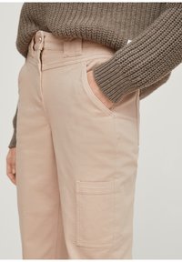 Pantaloni cargo rosa chiaro realizzati in misto cotone, dotati di tasche laterali e una vestibilità dritta, abbinati a un maglione lavorato a maglia marrone spesso e testurizzato.