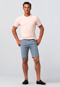 Light pink short-sleeve t-shirt with a pocket, paired with light blue shorts. Dark shoes complete the casual outfit.